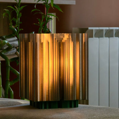 Decorative lamp with a striped design on a surface, with a plant in the background.